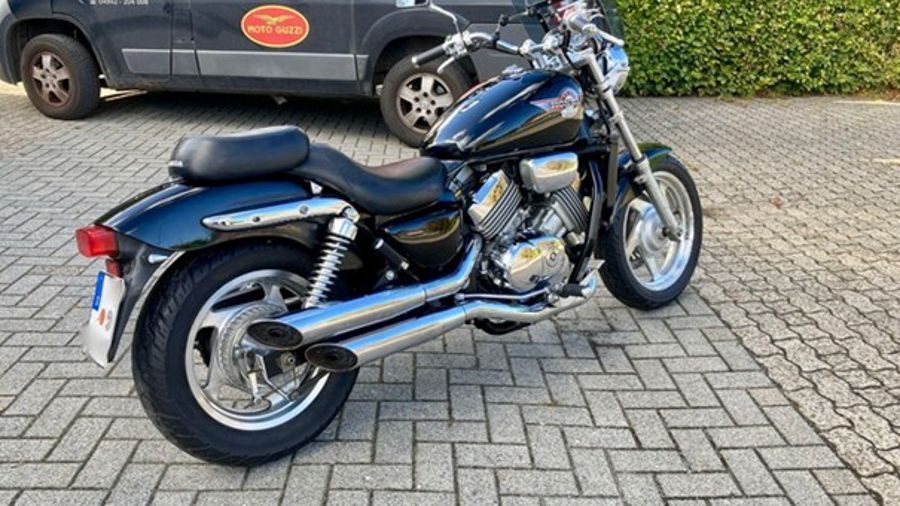 Schwarzes und verchromtes Honda-Motorrad auf Ziegelpflaster geparkt. Im Hintergrund ist ein dunkler Lieferwagen zu sehen.