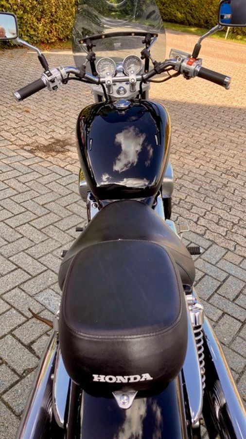 Schwarzes Honda-Motorrad, Draufsicht. Glänzender schwarzer Kraftstofftank, Chromakzente, Windschutzscheibe. Auf Ziegelpflaster.