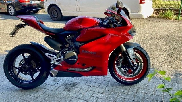 Auf einem Parkplatz steht neben einem weißen Lieferwagen ein rotes Motorrad.