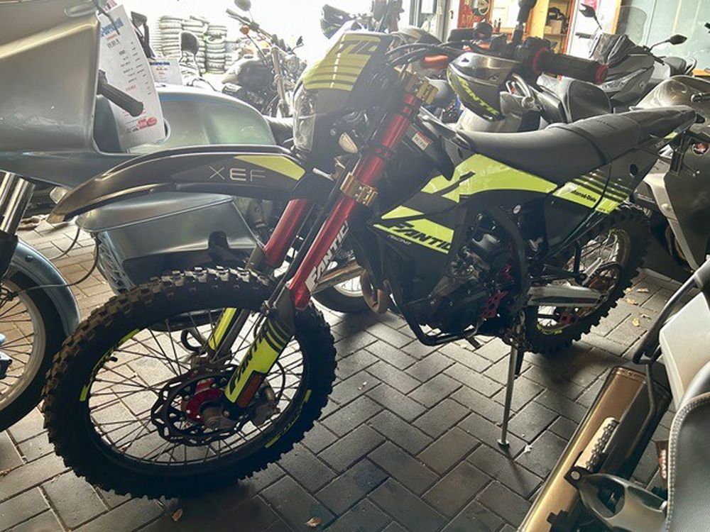 Drei Geländemotorräder in einem Ausstellungsraum, darunter ein gelb-schwarzes Dirtbike im Vordergrund.