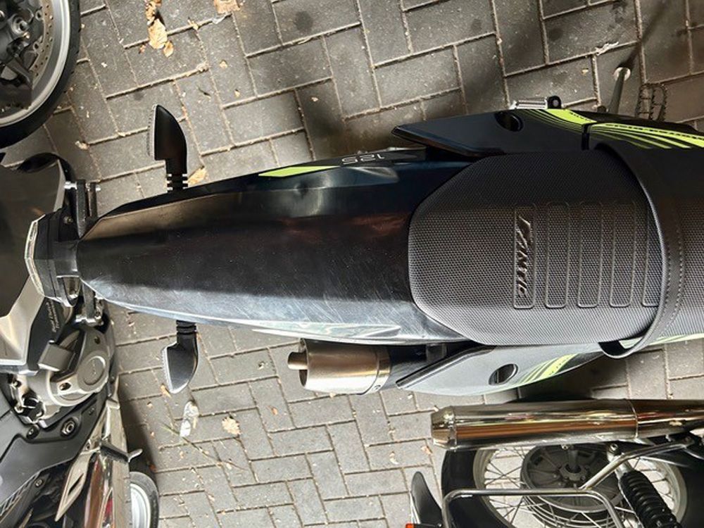 Draufsicht auf einen schwarzen Roller, der auf einer mit Ziegeln gepflasterten Straße geparkt ist.