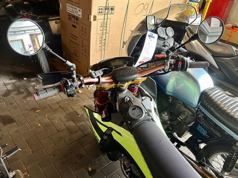 Motorradlenker und Spiegel in einer Garage, daneben ein weiteres Motorrad neben Pappkartons.