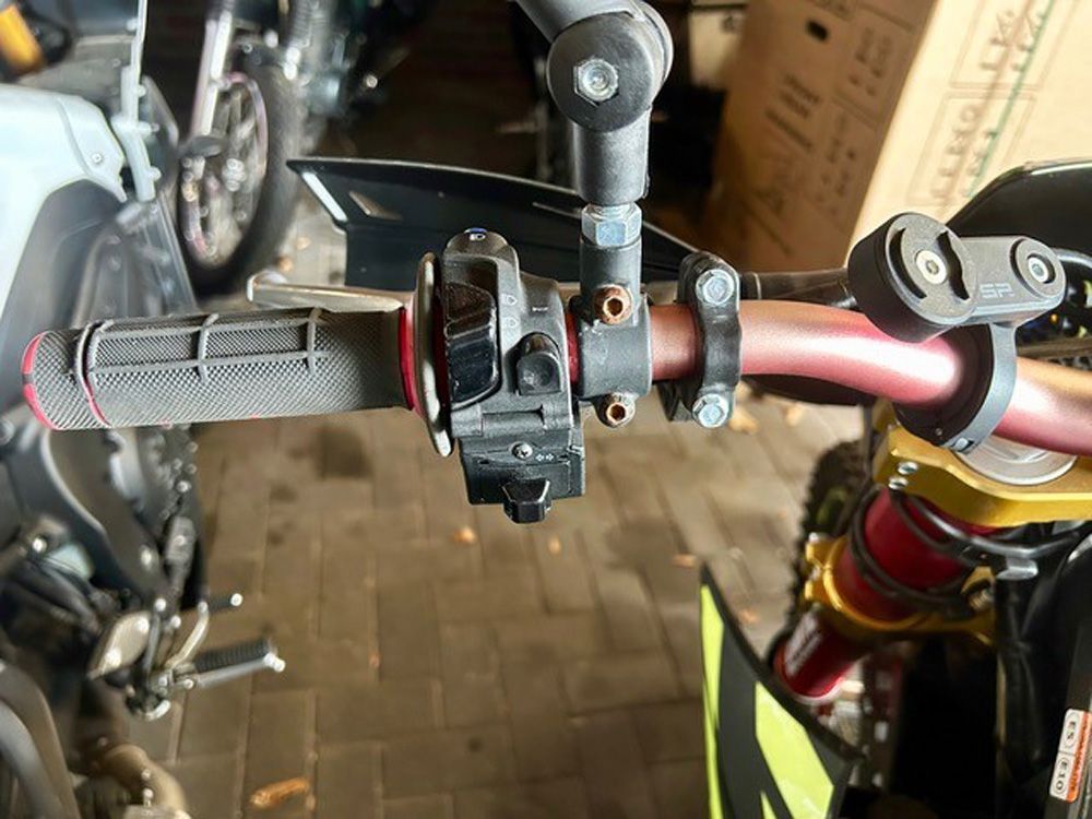 Nahaufnahme eines Fahrradlenkers mit schwarzem Griff, Bremshebel und montiertem Zubehör an einem roten Rahmen