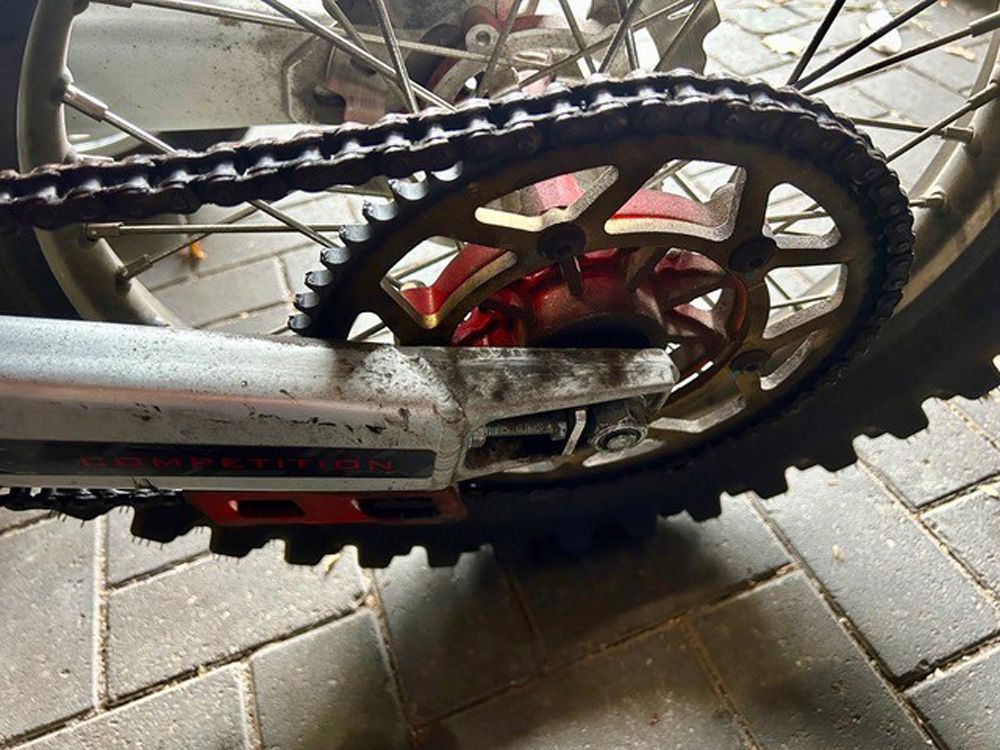 Nahaufnahme einer Fahrradkette mit hinterem Ritzel, rotem Kettenrad und Reifen auf Asphalt