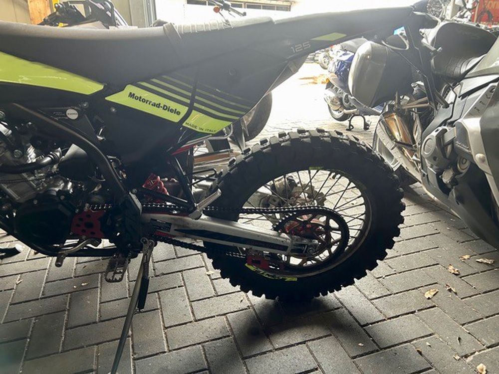 Zwei geparkte Dirtbikes auf einer mit Ziegeln gepflasterten Straße, eines schwarz und eines neongrün im Vordergrund.