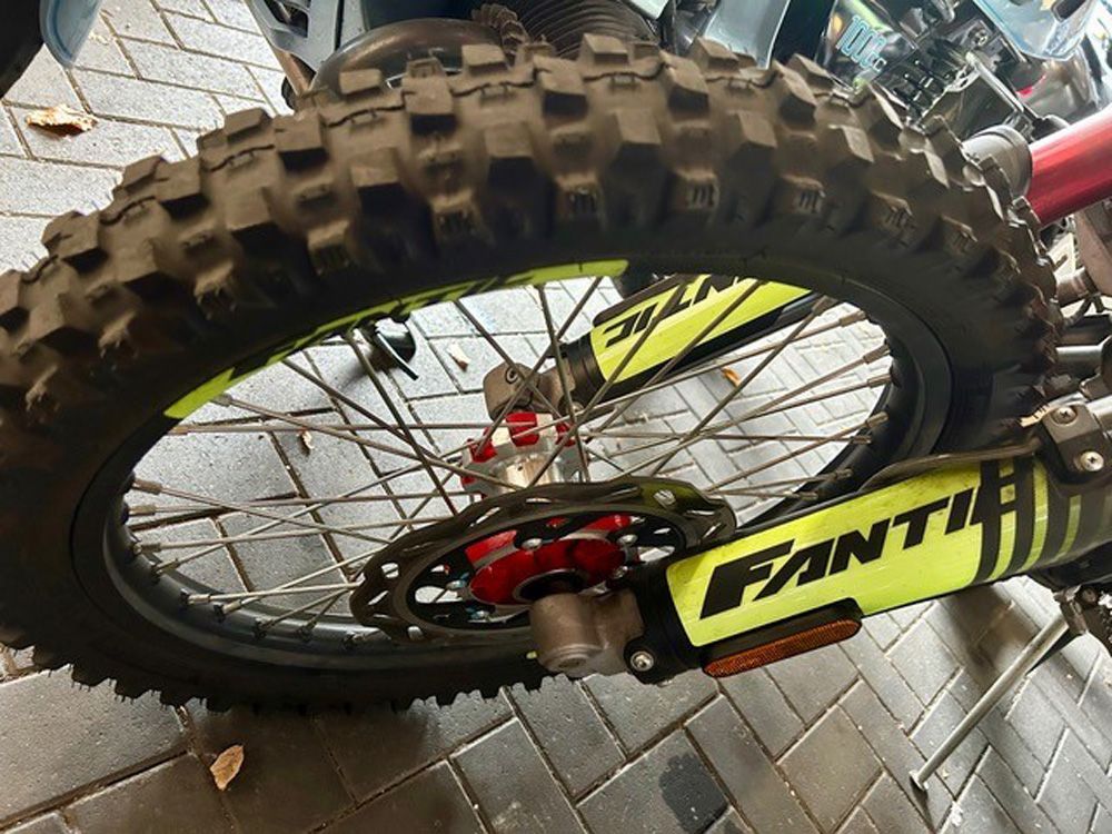 Nahaufnahme eines Dirtbike-Rads mit Stollenreifen und gelbem Fantic-Rahmen auf Asphalt.