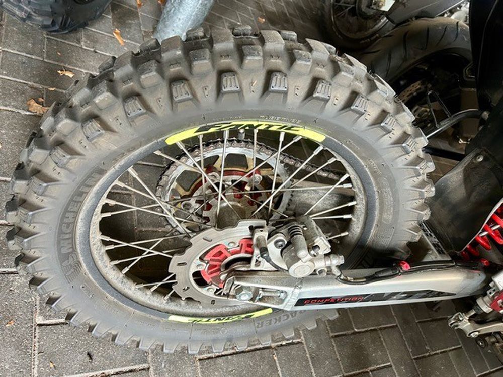 Nahaufnahme des Hinterrads und der Schwinge eines Dirtbikes, auf der der Stollenreifen und der Kettenantrieb zu sehen sind.