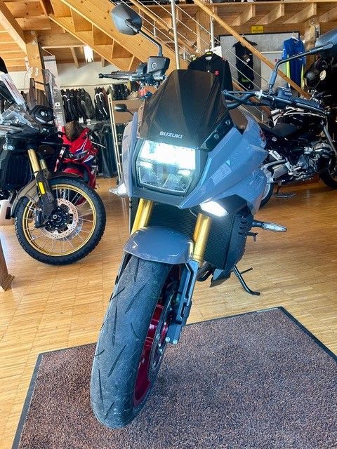 Schwarzes Sportmotorrad in einem Ausstellungsraum, Vorderansicht auf Holzboden, im Hintergrund weitere Motorräder.