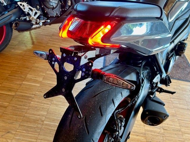 Rückansicht eines schwarzen Sportmotorrads mit rot leuchtenden Rücklichtern und einem breiten Hinterreifen