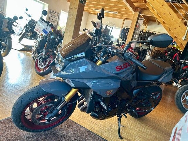 Ein rotes Sportmotorrad mit schwarzen Akzenten steht in einer Halle zwischen anderen Motorrädern.