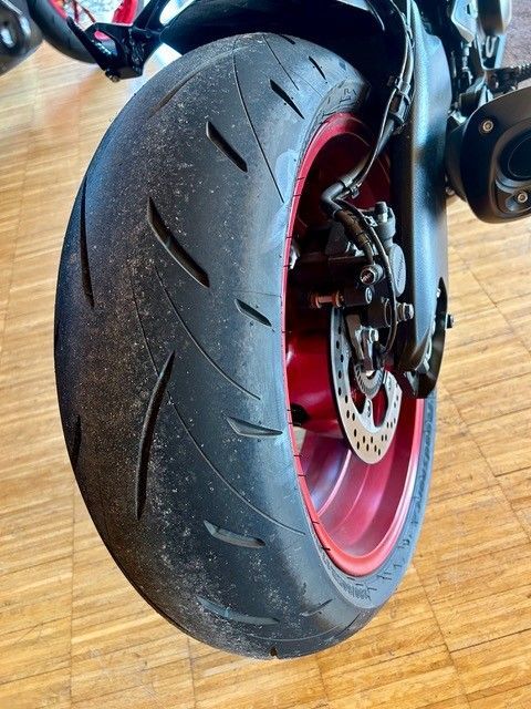 Nahaufnahme eines Motorradhinterreifens mit roter Felge und sichtbarer Bremsscheibe auf einem Holzboden