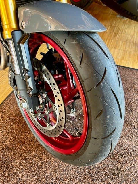 Nahaufnahme eines Motorradvorderrads mit roter Felge, schwarzem Reifen und grauem Schutzblech in einem Innenraum