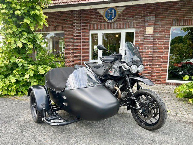 Schwarzes Motorrad mit Beiwagen parkt vor einem Backsteingebäude, in der Nähe befindet sich Grün.