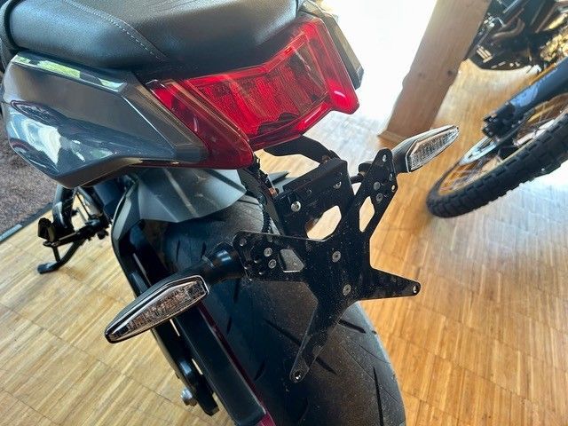 Rückansicht eines dunklen Motorrads mit rotem Rücklicht und Kennzeichenhalterung auf einem Holzboden