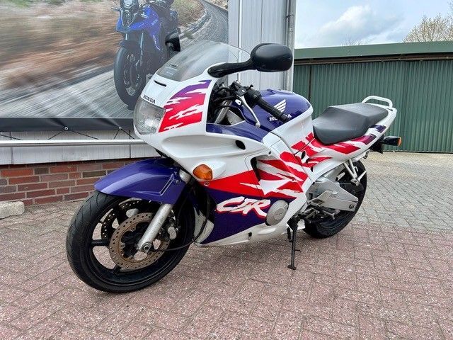 Ein blau-weiß-rotes Sportmotorrad parkt auf einem gepflasterten Platz vor einem Gebäude.