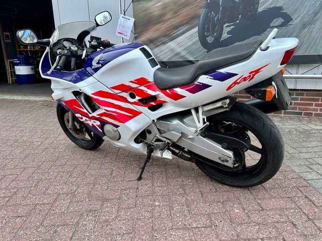Ein rot-weiß-blaues Sportmotorrad parkt auf einem gepflasterten Gehweg in der Nähe eines Glasfensters.