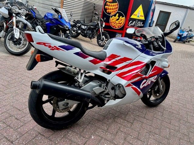 Ein weißes und ein rotes Sportmotorrad parken im Freien neben anderen Motorrädern.