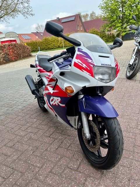 Ein weißes, rotes und blaues Sportmotorrad parkt auf einer gepflasterten Auffahrt in einem Wohngebiet.