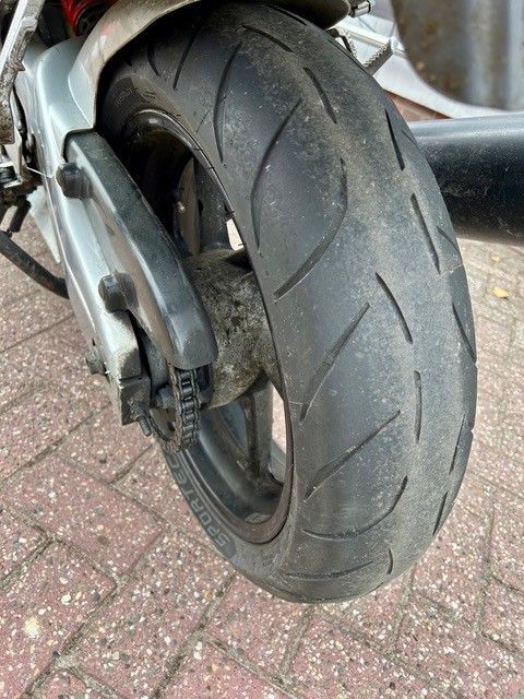 Nahaufnahme eines Motorradhinterreifens und -rads auf einem Ziegelpflaster, die abgefahrenes Profil zeigt.