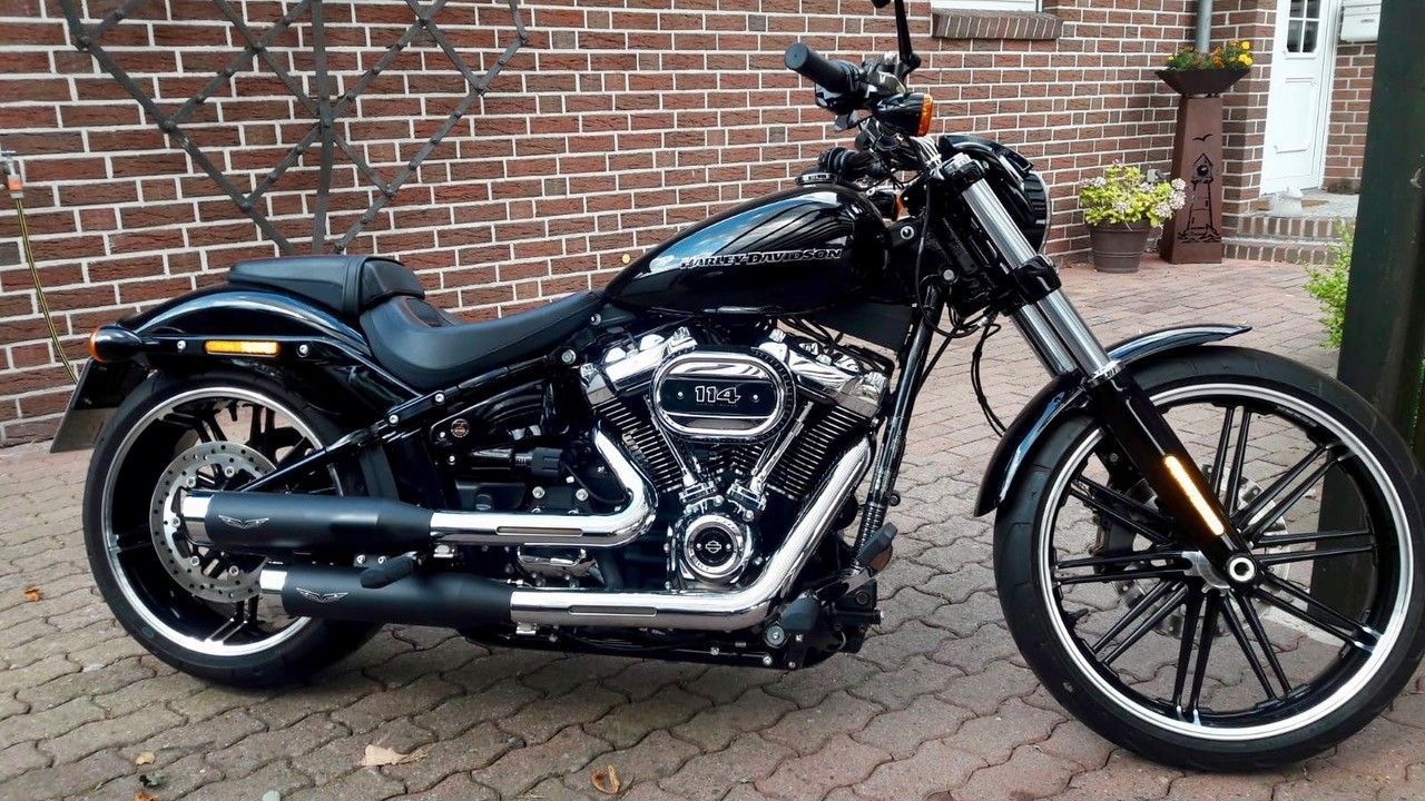 Schwarzes Cruiser-Motorrad parkt auf einer gepflasterten Auffahrt neben einer Backsteinmauer und dem Hauseingang.