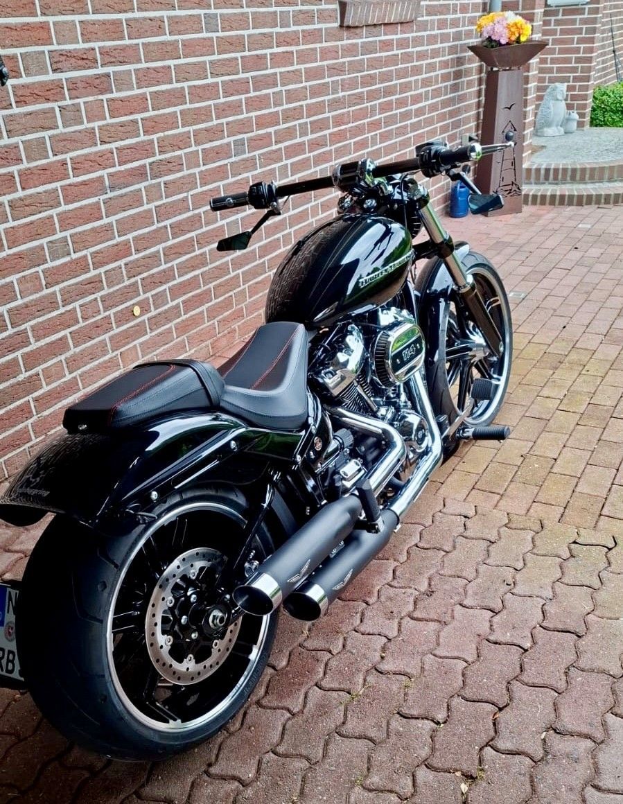 Ein schwarzes Custom-Motorrad parkt auf einer gepflasterten Auffahrt neben einer Backsteinmauer.