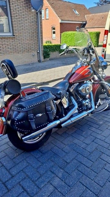 Ein rot-schwarzes Cruiser-Motorrad parkt auf einer gepflasterten Auffahrt in einem Wohngebiet.