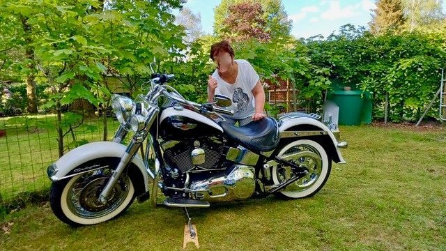 Frau sitzt auf einem schwarz-weißen Motorrad in einem grasbewachsenen Hinterhof