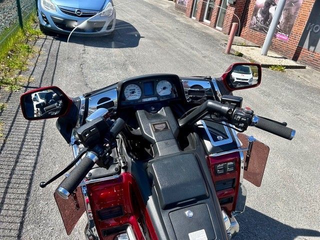 Blick aus dem Cockpit eines Motorrads auf einer Einfahrt, mit Spiegeln, Armaturenbrett und einem geparkten silbernen Auto davor.