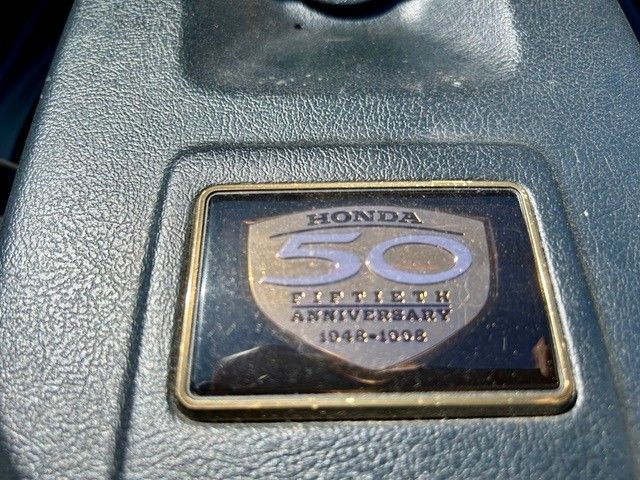 Nahaufnahme eines Honda-Emblems zum 50-jährigen Jubiläum auf einer grauen, strukturierten Oberfläche.