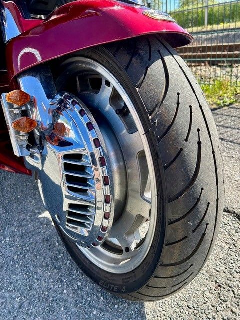 Nahaufnahme eines Motorradhinterrads und einer verchromten Nabe unter einem roten Schutzblech auf dem Asphalt.