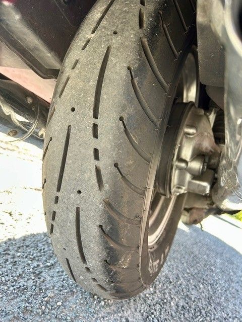 Nahaufnahme eines Motorradhinterreifens mit abgefahrenem Profil auf Asphalt, die Rad und Bremsanlage zeigt.
