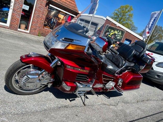 Ein rotes Tourenmotorrad mit Chromdetails und Windschutzscheibe steht im Freien neben einem Gebäude.