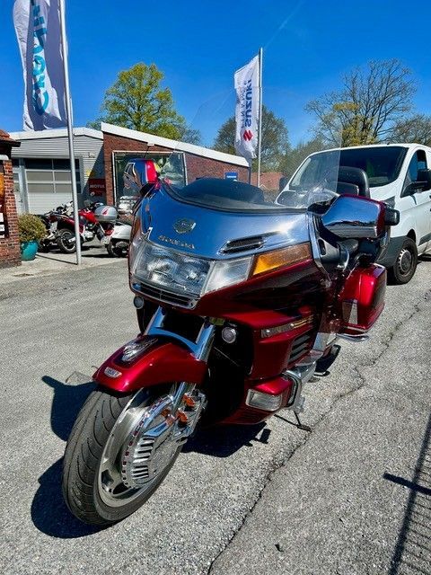 Ein rotes Tourenmotorrad steht im Freien auf dem Gelände eines Händlers; daneben stehen Flaggen und ein weißer Lieferwagen.