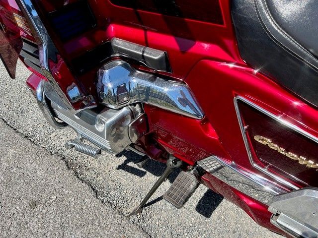 Nahaufnahme des verchromten Motors, Auspuffs und Trittbretts eines roten Motorrads auf dem Asphalt