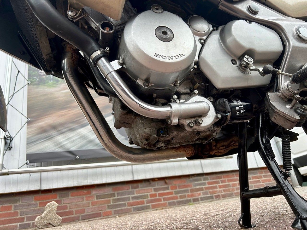 Nahaufnahme eines Motorradmotors und -auspuffs, montiert auf einem Ständer über einem Ziegelpflaster.