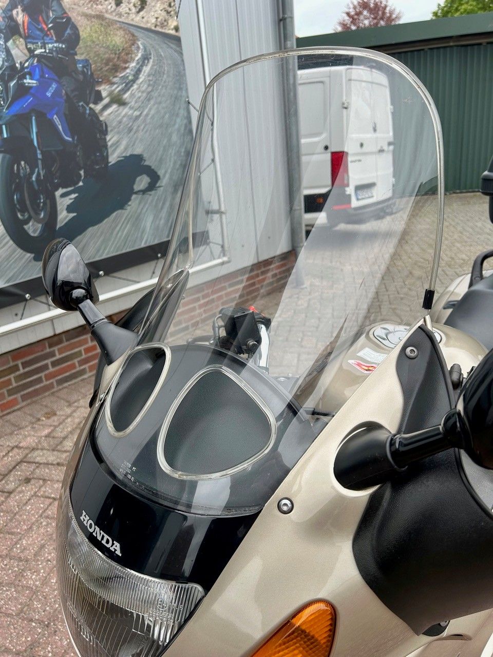 Ein Motorrad mit hoher, durchsichtiger Windschutzscheibe parkt neben einem weißen Lieferwagen und einem Backsteingebäude.