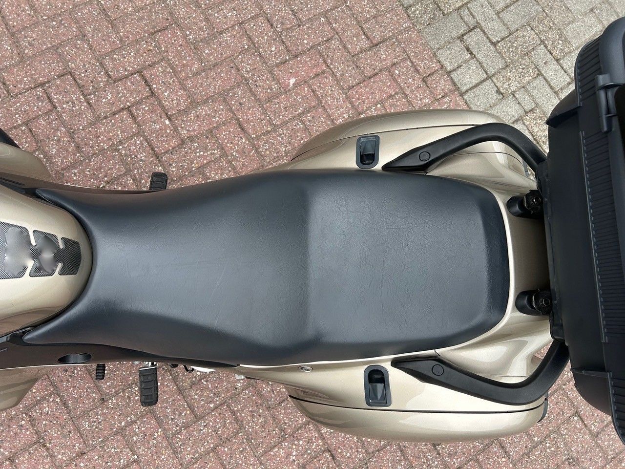 Draufsicht auf einen schwarzen Motorradsitz und das Heckteil, die auf einem gepflasterten Gehweg abgestellt sind.