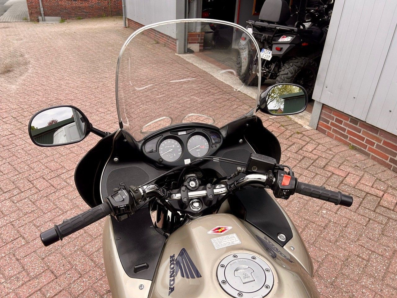 Armaturenbrett und Windschutzscheibe eines Motorrads, das auf einer gepflasterten Auffahrt vor einem Gebäude geparkt ist.