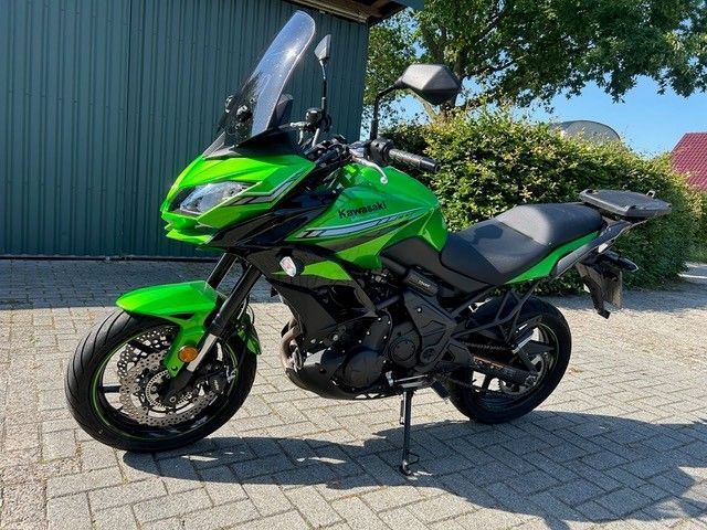 Ein grünes Kawasaki-Motorrad parkt auf einer gepflasterten Auffahrt neben einem Gebäude und Bäumen.