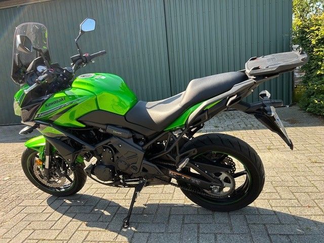 Ein grünes Sportmotorrad parkt auf dem Bürgersteig neben einer Wellblechwand.