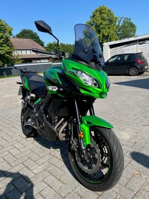 Grünes Sportmotorrad, mit Windschutzscheibe und Seitenspiegeln, parkt auf einem gepflasterten Parkplatz unter sonnigem Himmel.