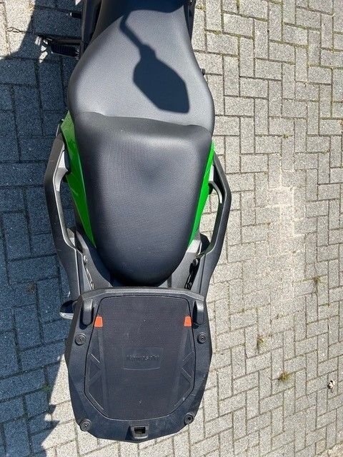 Draufsicht auf ein schwarz-grünes Motorrad, das auf grauem Backsteinpflaster geparkt ist.