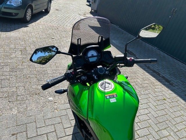Grünes Motorrad, geparkt auf einer gepflasterten Auffahrt neben einer Mauer, Ansicht von vorne.