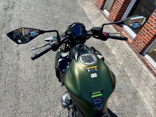 Grünes Motorrad, geparkt auf einer gepflasterten Straße neben einem Backsteingebäude, Ansicht von oben.