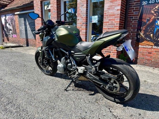 Ein grün-schwarzes Motorrad parkt im Sonnenlicht vor einem Backsteingebäude.