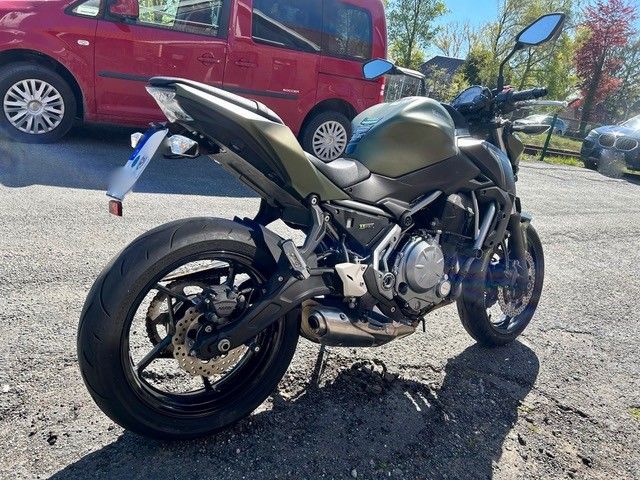 Schwarzes Sportmotorrad parkt auf Asphalt, im Hintergrund ist ein roter SUV zu sehen.