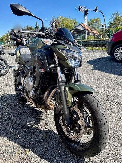 Schwarzes Sportmotorrad parkt auf Kies in einer sonnigen Einfahrt, Vorderansicht mit Häusern und Autos im Hintergrund