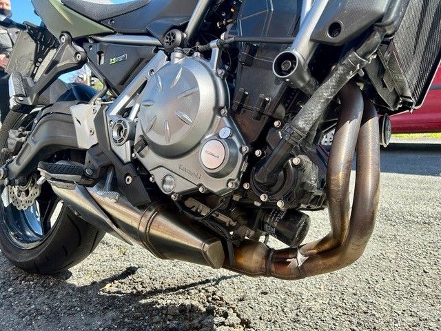 Nahaufnahme eines Motorradmotors und Auspuffrohren auf Schotter, die Metallteile und das Hinterrad zeigt.