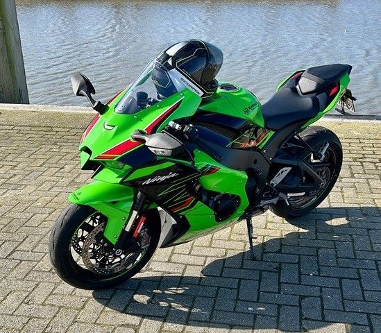 Ein grünes Motorrad ist auf einem gepflasterten Gehweg neben einem Gewässer geparkt.