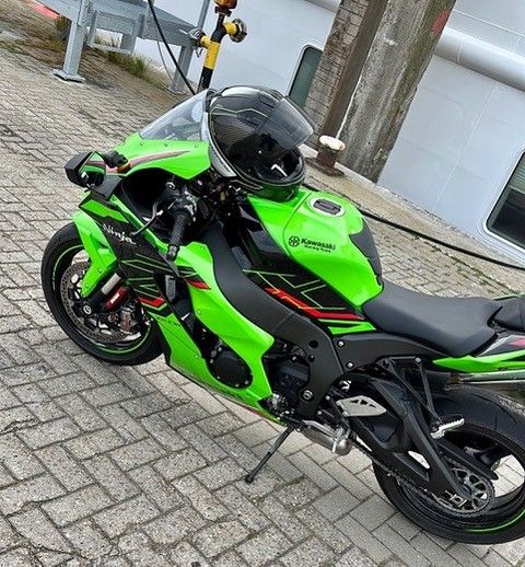 Ein grünes Motorrad mit einem Helm darauf ist auf einem gepflasterten Gehweg geparkt.